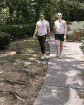 two men walking down a sidewalk with one wearing a t-shirt that says ' armani ' on it