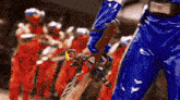 a person in a blue jumpsuit is holding a sword in front of a group of people in red jumpsuits .