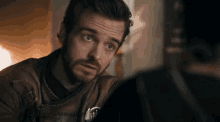 a man with a beard is wearing a brown leather jacket and looking at something