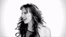 a black and white photo of a woman laughing with her hair blowing in the wind