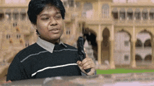 a man in a black sweater holds a gun in front of a building