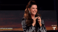 a woman in a black and silver jacket is smiling and holding her fist up .