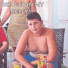 a shirtless boy is sitting at a table with a box of fruit juice in his hand .
