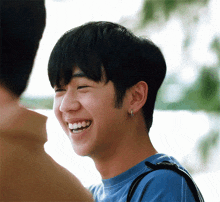 a young man wearing a blue shirt and earrings smiles for the camera