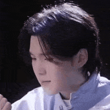 a close up of a young man 's face with long hair and a white shirt .