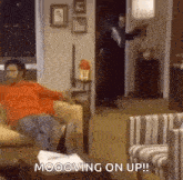 a man is sitting on a couch in a living room with the words `` mooowing on up '' .