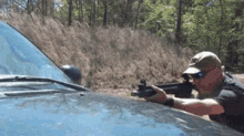a man is holding a gun in front of a car .