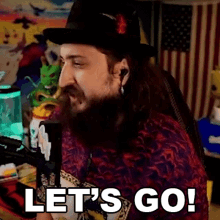 a man with a beard wearing a hat and ear buds is saying let 's go !
