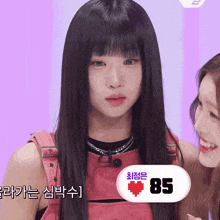 a girl with long black hair is standing next to another girl with a sign that says 85