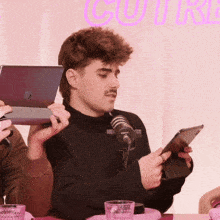 a man sitting at a table with a microphone and a tablet in his hands