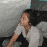 a woman in a white shirt smiles while sitting in a tent
