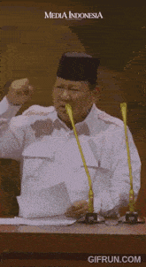 a man in a white shirt is sitting in front of a group of people with media indonesia on the bottom