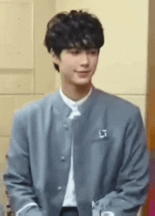 a young man wearing a gray jacket and a white shirt is smiling .