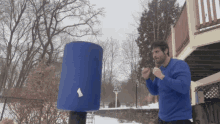 a man in a blue sweater is standing in front of a blue cylinder with a white triangle on it