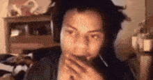 a man with dreadlocks is wearing headphones and covering his mouth with his hands .