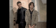 a man in a leather jacket is standing next to a woman in a trench coat .