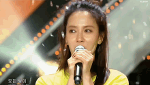 a woman in a yellow shirt singing into a microphone with the word elleigh on the bottom right