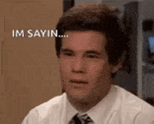 a man in a suit and tie is making a funny face and saying `` im sayin '' .