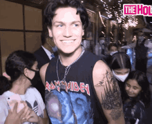 a man wearing a iron maiden tank top smiles in front of a crowd