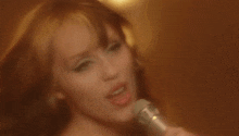 a woman is singing into a microphone in a close up of her face .