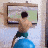 a young boy is standing on a blue exercise ball in front of a television .