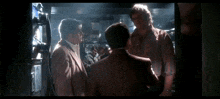 a group of men are standing next to each other in a dark room talking to each other .