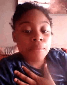 a young boy in a blue shirt is making a funny face with his hand on his chest