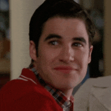 a man wearing a red sweater and plaid shirt smiles for the camera