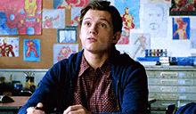 a young man is sitting at a desk in a classroom with drawings of iron man on the wall behind him .
