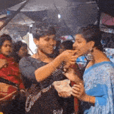 a man in a black shirt is feeding a woman in a blue saree some food