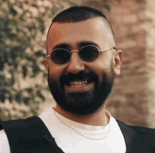 a man with a beard wearing round sunglasses and a white shirt