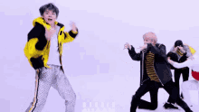 a group of young men are dancing in front of a white background . one of the men is wearing a yellow jacket .