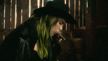 a woman with green hair wearing a black hat smoking a cigarette