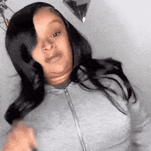 a woman with long black hair is making a funny face while wearing a grey hoodie .