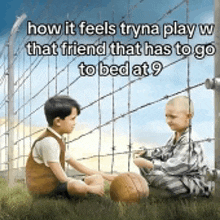 two children are sitting in the grass with a soccer ball in front of a barbed wire fence ..