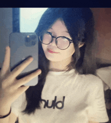 a girl wearing glasses takes a selfie with her phone while wearing a t-shirt that says hud