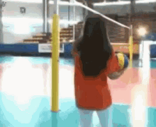 a girl in a red shirt is holding a volleyball in front of a volleyball net