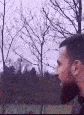 a man with a beard is standing in front of trees in a park .