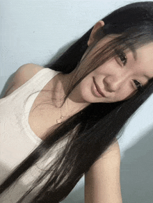 a woman with long black hair is wearing a white tank top and necklace