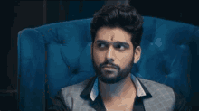a man with a beard is sitting in a blue chair looking at something .