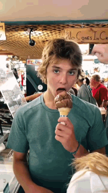 a boy is eating an ice cream cone in front of a sign that says no cones in cre