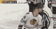a hockey player in a blackhawks jersey is being helped by a referee on the ice
