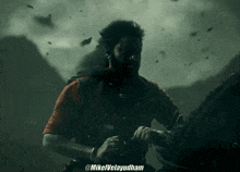 a man in a red shirt is standing in a dark room with the name mikelvelayudham on the bottom