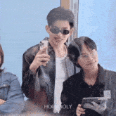 a man wearing sunglasses holds a cell phone next to another man with glasses