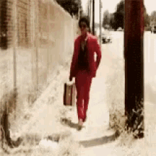 a man in a red suit is walking down a sidewalk holding a suitcase .