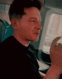 a man in a black shirt is sitting in a car looking out the window