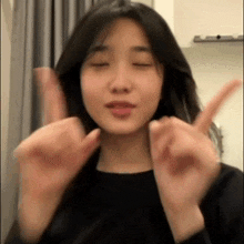 a woman is making a peace sign with her hands while looking at the camera .