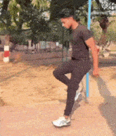 a man in a black shirt and black pants is standing on one leg .