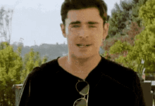 a man wearing sunglasses and a black shirt is smiling and looking at the camera .