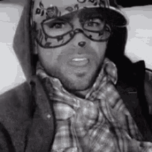 a black and white photo of a man wearing glasses , a hat , and a plaid shirt .